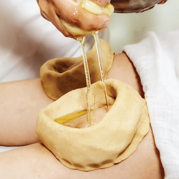 Therapist performing a Jannu Basti knee treatment